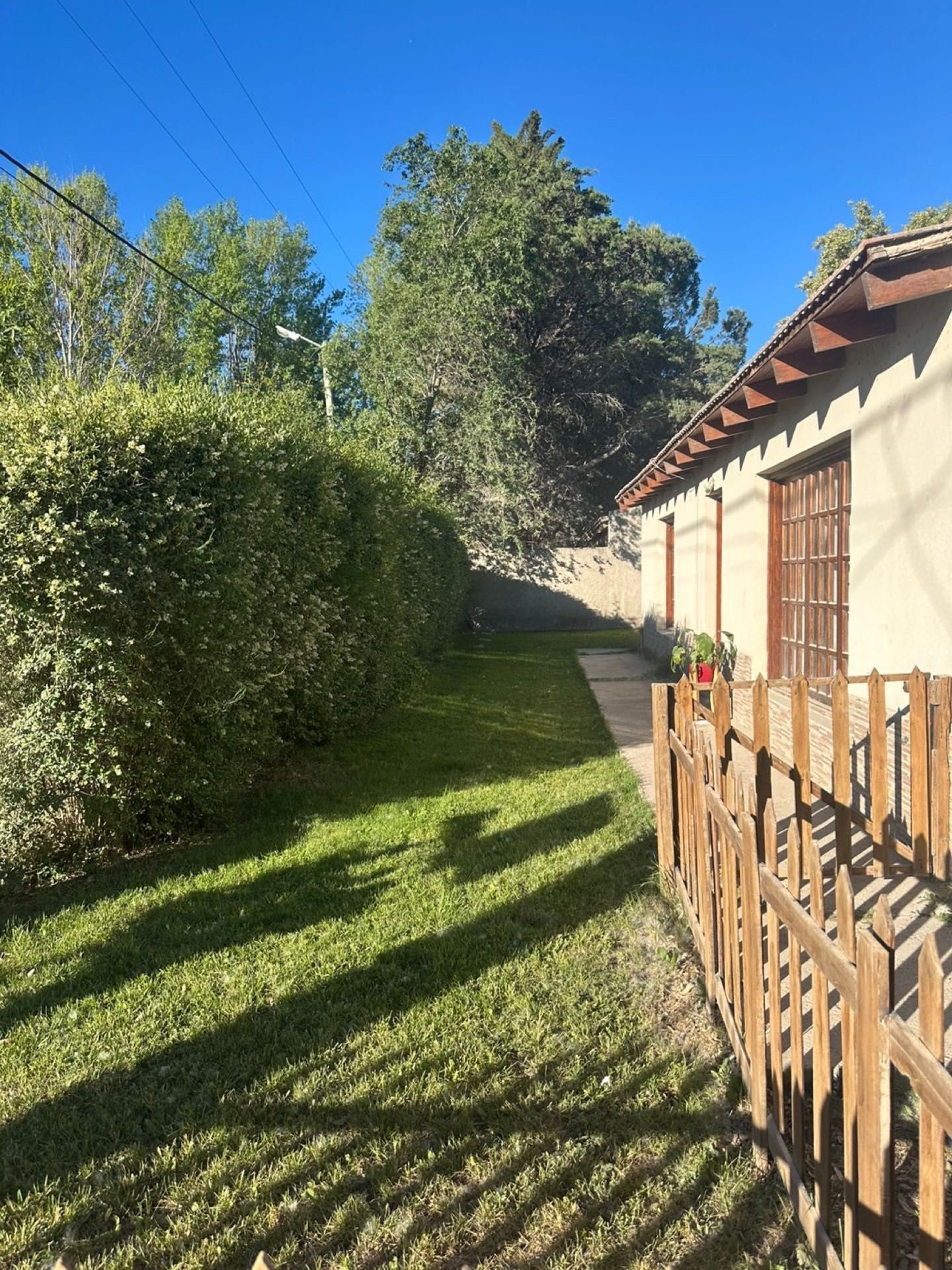 Costado de la casa con césped y cerquita de madera